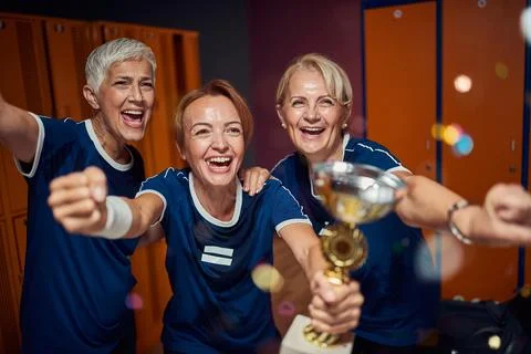 Team of two senior and one young women in dressing room, holding golden cup.. Stock Photos