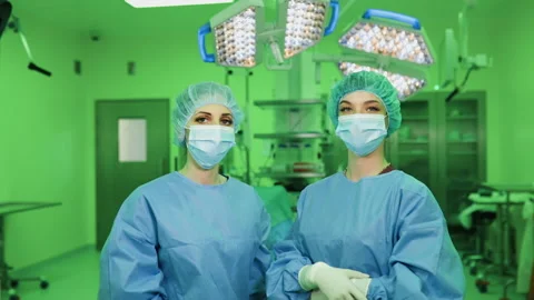 Team of two young female doctors in medical face masks, gloves and caps in Stock Footage