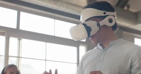 Team watching Asian man starting VR headset demo, raising right hand, testing Stock Footage 339983493