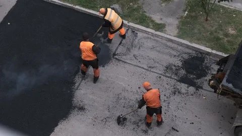 Team of workers in orange vests manually spreading fresh asphalt on the roa.. Stock Footage 339802197