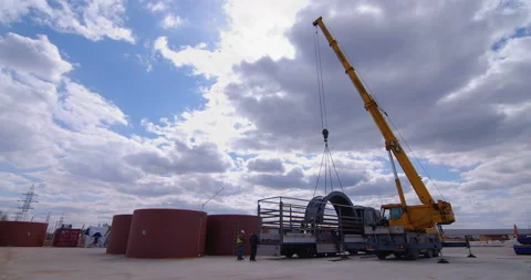 A team of workers in overalls and helmets help a large yellow truck crane unload Stock Footage 161963976