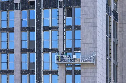 A team of workers on a suspended cradle performs edging facade work in a mode Stock Photos