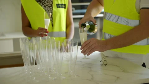 Team in yellow high visibility vests celebrating deal pouring Champagne Stock Footage 224477933