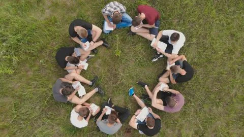 Teamwork concept. A group of high school students sit on the grass in a circle Stock Photos