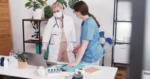 Teamwork concept. Young nurse in blue scrubs consults, looks at laptop with Stock Footage 152550872