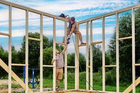 Teamwork during house framing as young worker passes cordless drill to coll.. Stock Photos