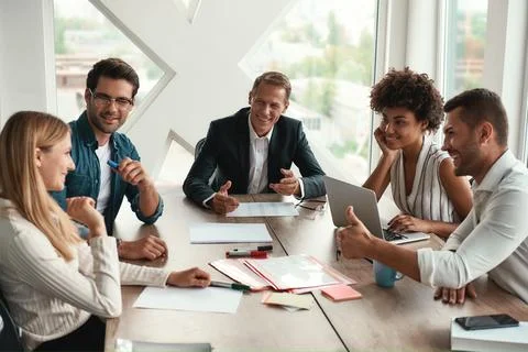 Teamwork. Multicultural team discussing something and smiling while sitting at Stock Photos
