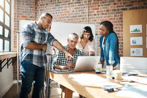 Teamwork simplifies the task. a group of colleagues using a laptop together in a Stock Photos