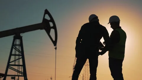 Teamwork. Two workers in hard hats at sunset. Working oil pump silhouette. Two Stock Footage 232330695