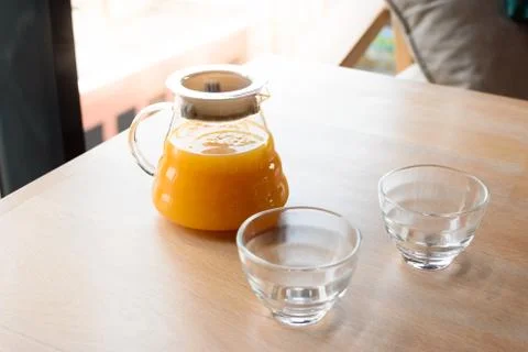 Teapot of orange fruit tea and two glass cups in a wooden table in a cafe. Stock Photos