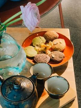 Teapot, two teacups, plate of assorted cookies, physalis and pink ranunculus Stock Photos