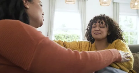 Tears falling making mother reaching across sofa at home and hugging daughter Stock Footage 336609117