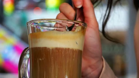 A teaspoon removes the foam from the coffee glas in a glass of ayrish Stock Footage 80241543