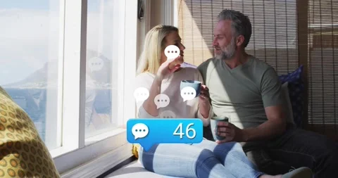 Tech couple sitting sea-view nook sipping mugs tracking blue bubble appearing, Stock Footage 318688800