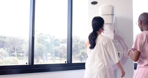 Tech explaining and guiding gowned patient positioning at mammogram paddle in Video stock 344644953