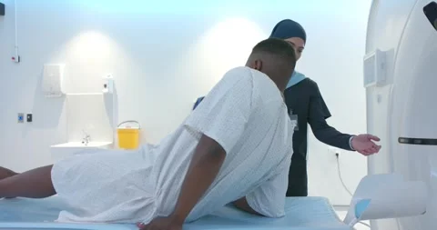 Tech gesturing, hijab-clad tech guiding African American male lying back onto CT Stock Footage 344850987