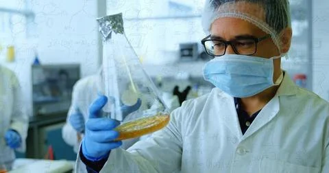 Tech holding flask up inspecting amber liquid for test comparing foil flask with Stock Photos