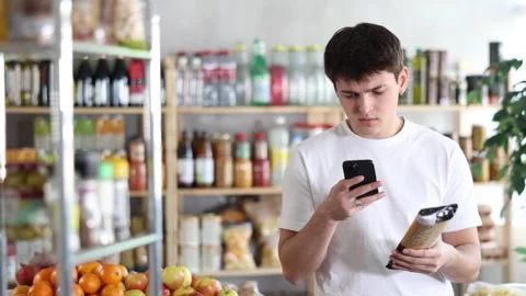 Tech-savvy young shopper scanning spaghetti package with smartphone, using Stock Footage 346122227