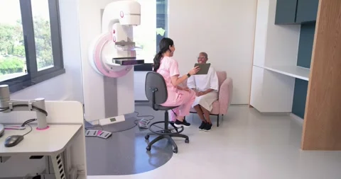 Tech in scrubs holding tablet explaining mammogram prep to senior African Stock Footage 336715790