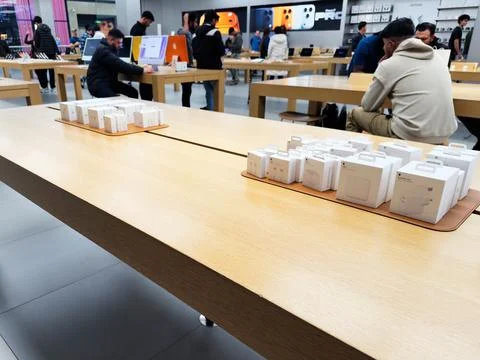 Tech store customers browse packaged devices on wooden tables in a bright A.. Foto stock
