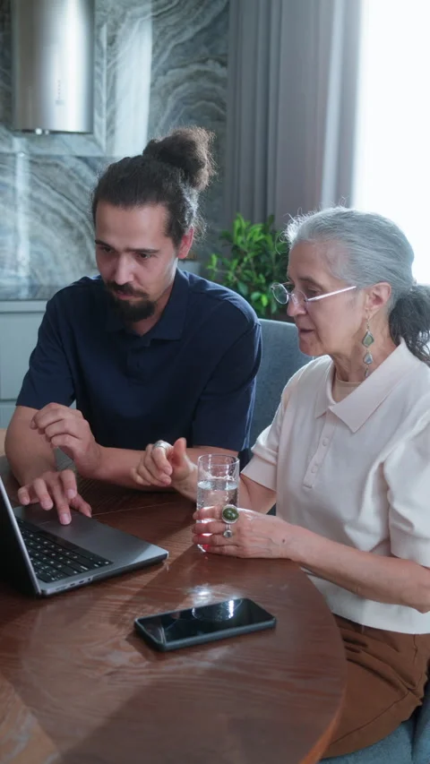Tech Tutor Explaining Laptop Basics to Elderly Woman at Home Stock Footage 337007950
