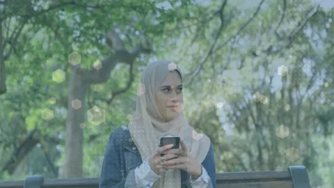Tech woman tapping phone scrolling in park glancing offscreen hex bokeh overlay Stock Footage 333949554