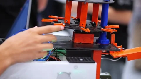 Tech worker handles wires near moving orange robotic assembly Stock Footage 345402205
