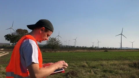 Technical engineer scrolling info on tablet near wind towers Stock Footage 98149459