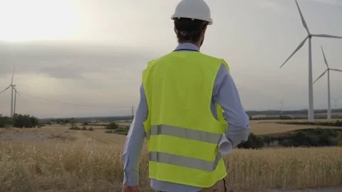 Technical engineer walks holding blueprint in wind farm. Professional technician Stock Footage 240083739