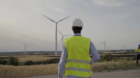 Technical engineer walks holding blueprint in wind farm. Professional turns to Stock Footage 244954998