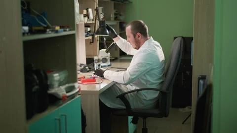 Technician Adjusts Desk Lamp and Works Under Microscope in Laboratory Stock Footage 284358965