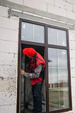 Technician adjusts plastic window in brick wall, installation process, regu.. Stock Photos