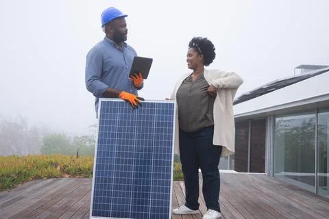 Technician and homeowner inspecting solar panel on rooftop deck with blue hard Stock Photos