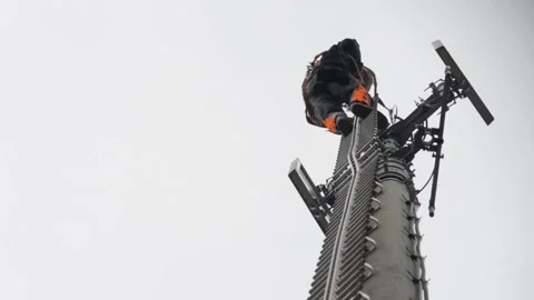 Technician Climbing Cell Tower for Maintenance on Overcast Day Stock Footage 334053820