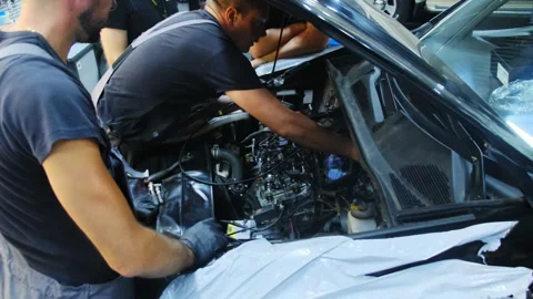 Technician with colleagues checks car using voltmeter in shop Stock Footage 317632178