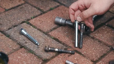Technician comparing worn and new brake caliper guide pins during car repair Stock Footage 335368893