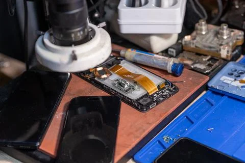 A technician conducts a battery replacement for a mobile phone on a workbench Stock Photos