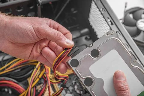 A technician is connecting a SATA power cable to a hard drive during a computer Stock Photos