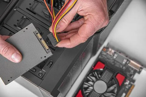 A technician connects a power cable to a solid state drive during a computer Stock Photos
