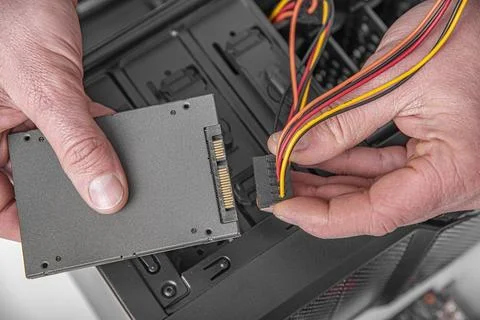 A technician connects a power cable to a solid state drive during a computer Stock Photos
