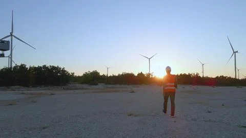 Technician engineer walking inside windmill wind turbine farm at sunset Foto stock