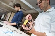 Technician Examining Drone While Coworker Using Laptop Computer In Office Stock Photos