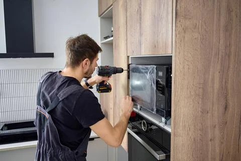 Technician Fixing Microwave Oven in Kitchen Cabinet Stock Photos