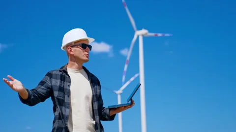 Technician gesturing while holding tablet near wind turbine. A man wearing a Stock Footage 343377213
