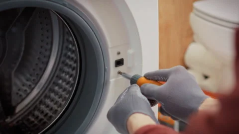 A technician in gloves methodically unscrews bolts from the washing machine Stock Footage 340786311