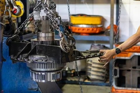 Technician hand guides heavy planetary gear assembly suspended by chains in.. Stock Photos