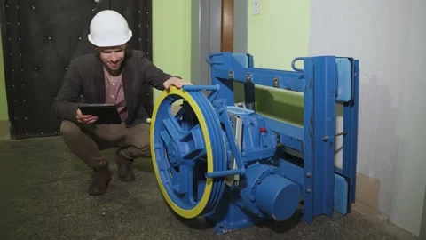 Technician in helmet checks parameters of new elevator equipment in tablet. Stock Footage 199971237