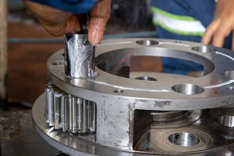 Technician inserts greased pinion pin into planetary gear carrier in indust.. Stock Photos