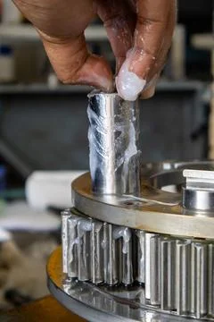 Technician inserts greased pinion pin into planetary gear carrier assembly .. Stock Photos