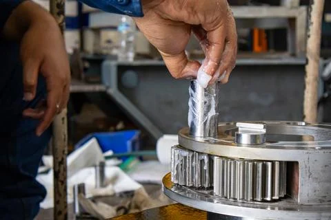 Technician inserts greased pinion pin into planetary gear carrier assembly .. Stock Photos